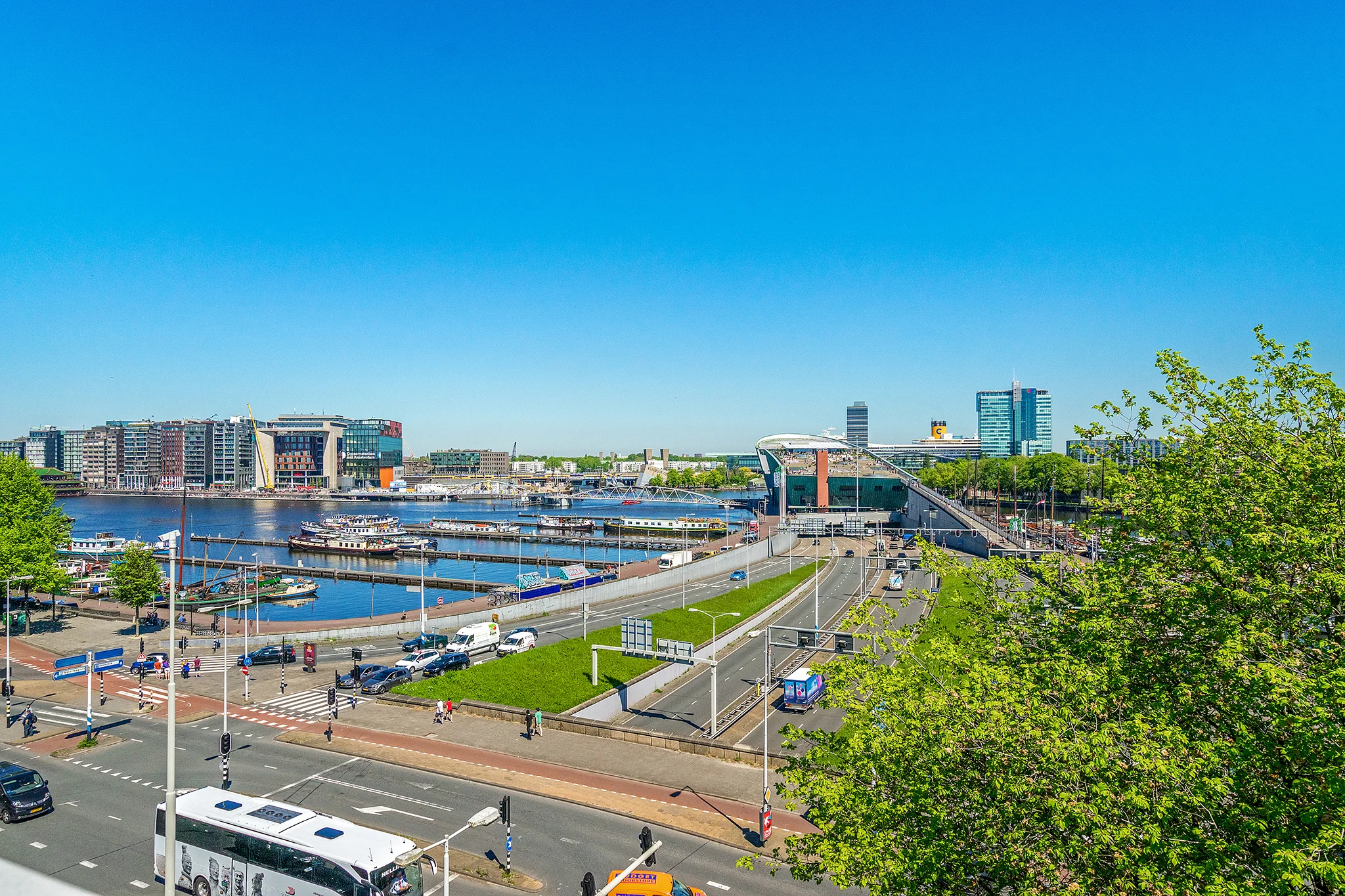 Uitzicht op de Prins Hendrikkade in Amsterdam met het IJ, boten en moderne gebouwen op de achtergrond.